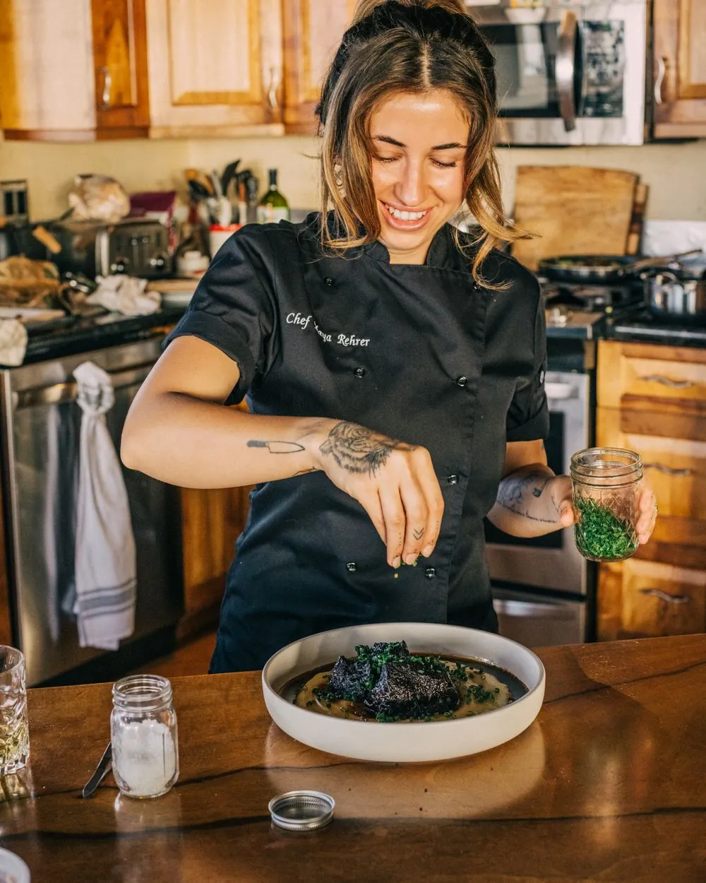 Chef Maya Rehrer laughing while garnishing braised short rib with chives