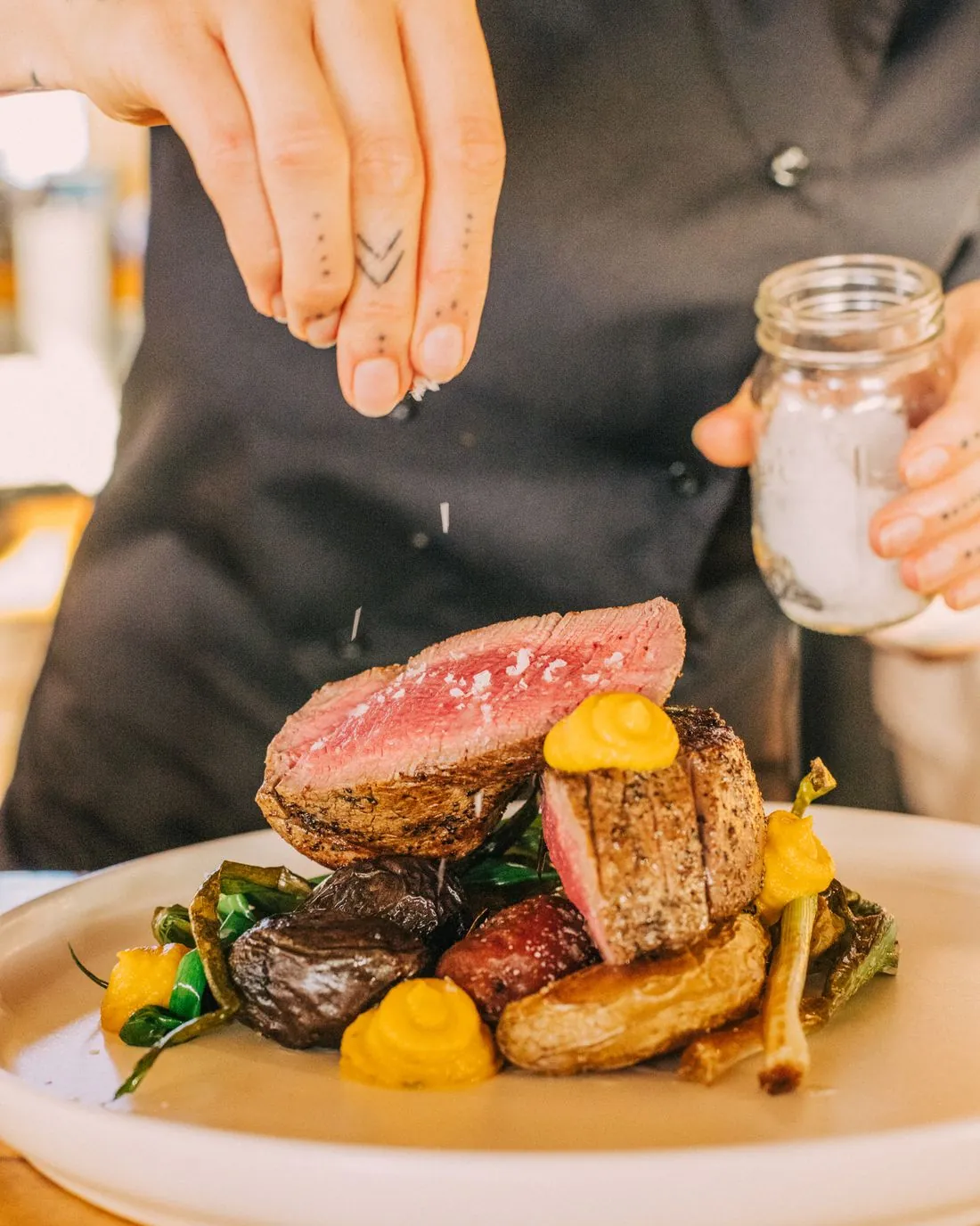 Flaky salt falling onto sliced steak with roasted potatoes