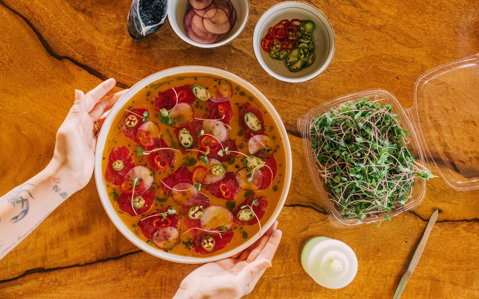 Chef Maya holding a platter of tuna crudo beside bowls of garnishes